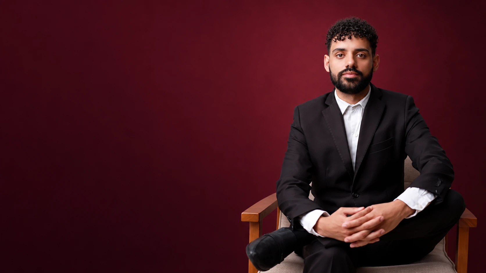 Tales Caetano em retrato sentado, em composição ilustrativa de estúdio com fundo vinho